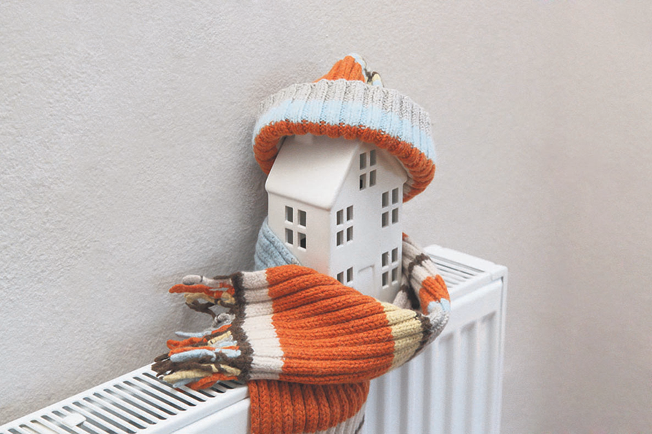 Kleines Modell eines Hauses mit Schal und Mütze auf einem Heizkörper.